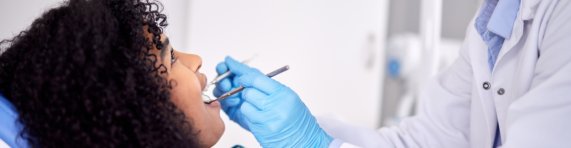 dentist's gloved hand using dental tool in woman's mouth